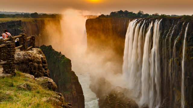 Victoria falls sunset with orange sun and tourists